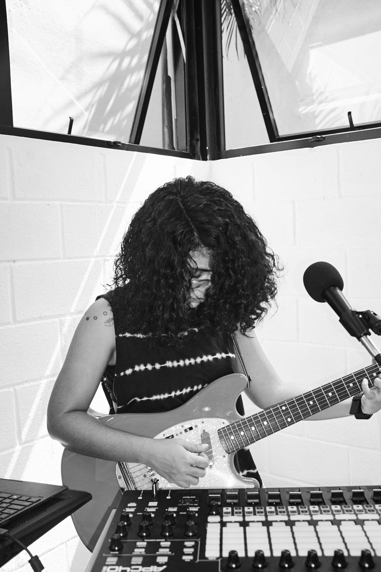 Plano cenital de Maria Lunares tocando la guitarra sobre el controlador, con el pelo cubriéndole la cara y el micrófono al lado.