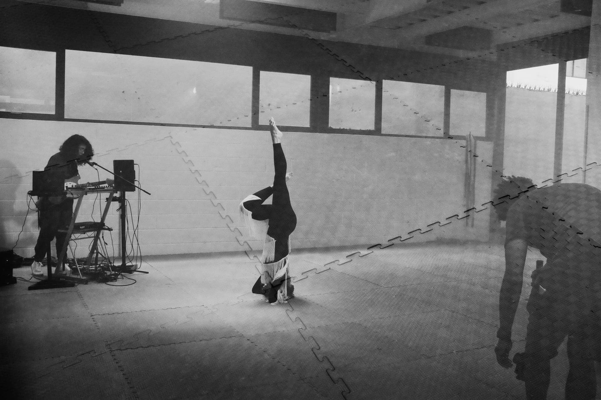 Plano general de la sala: la bailarina en vertical sobre la cabeza y Maria Lunares tocando junto a la pared del fondo.