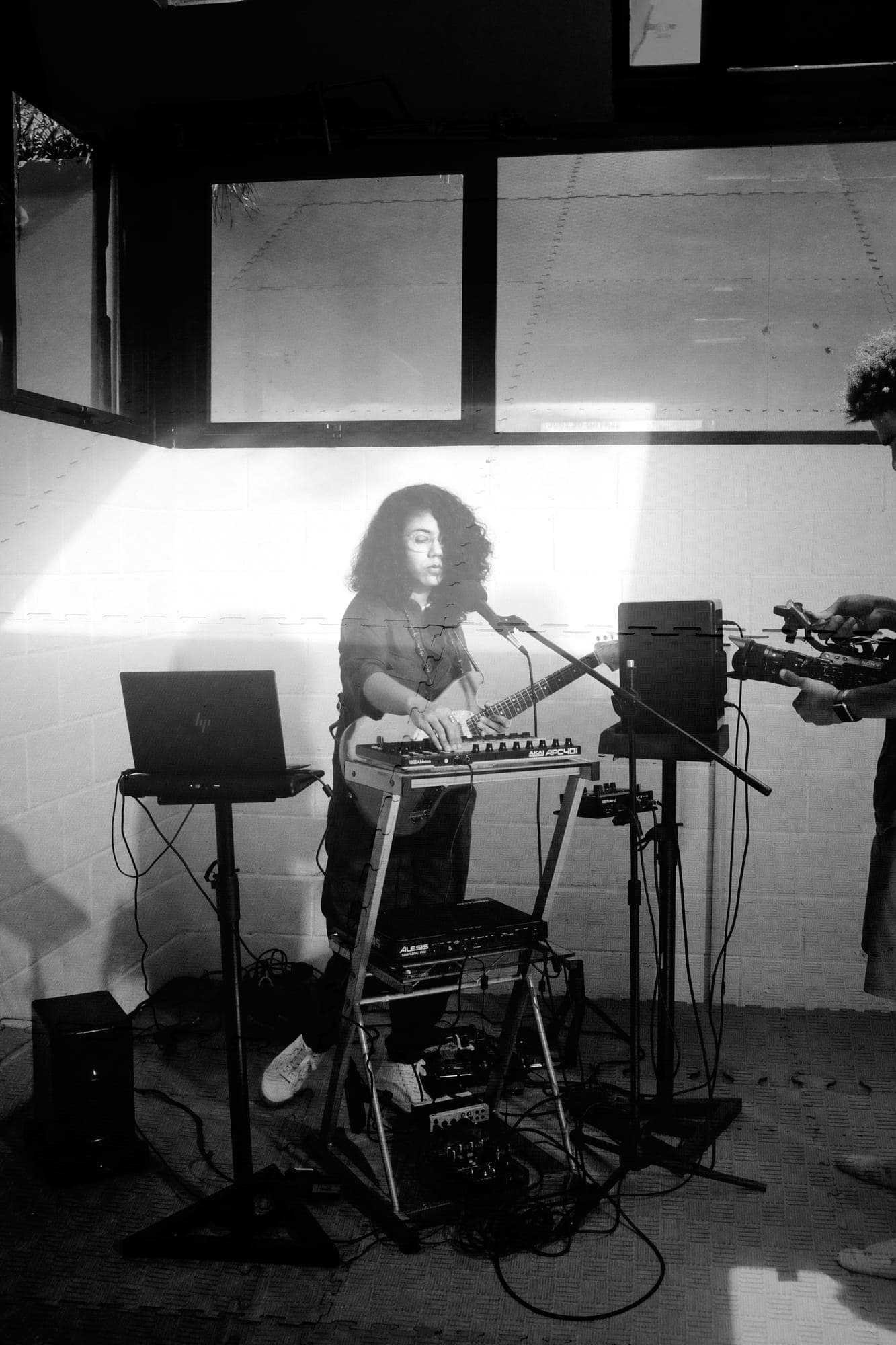 Doble exposición: Maria Lunares de pie ante su equipo (portátil, controlador y guitarra) con un cámara al borde del encuadre.