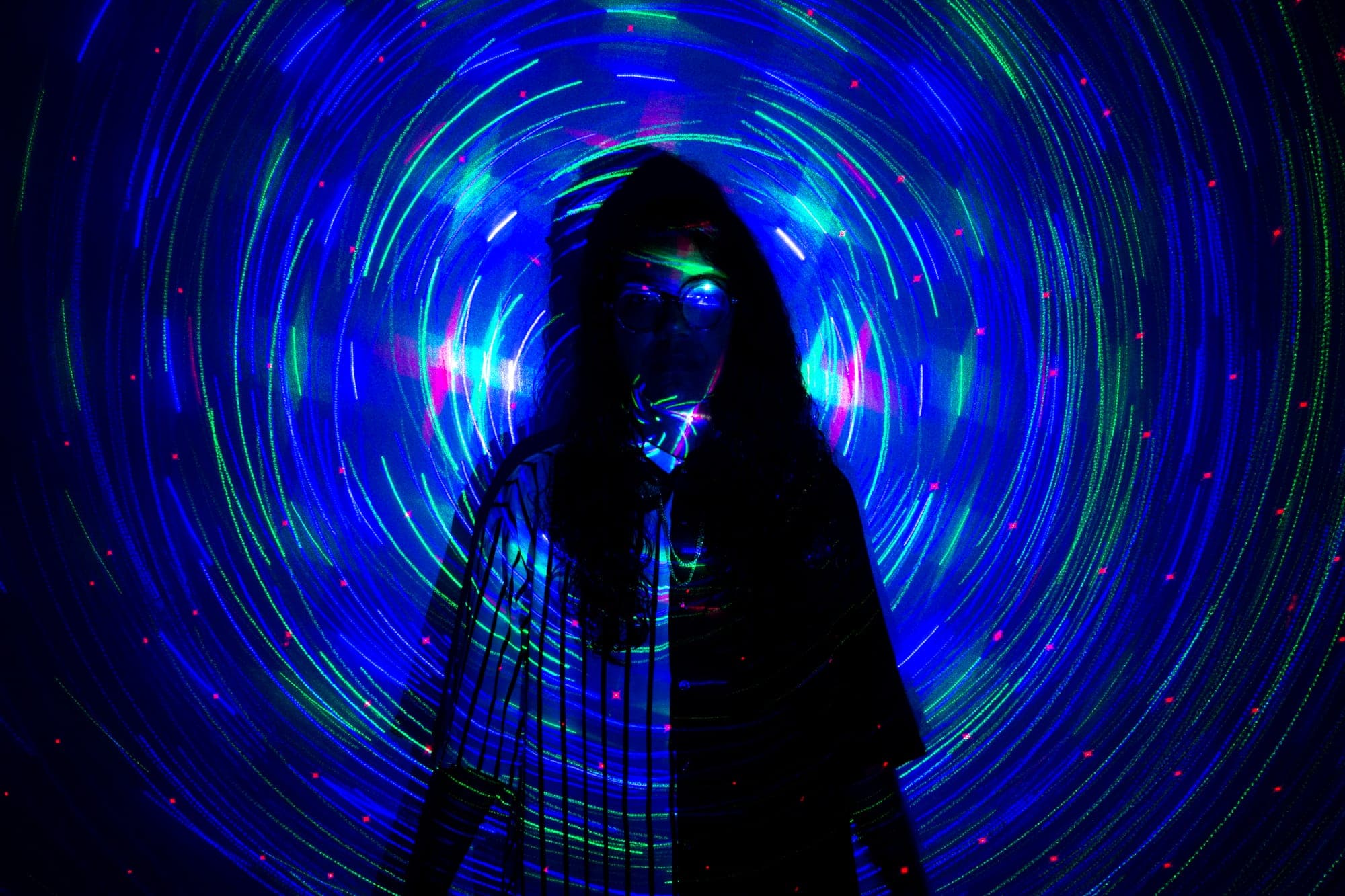 Silueta recortada contra una espiral de estelas de luz azul y verde, hecha con exposición larga.