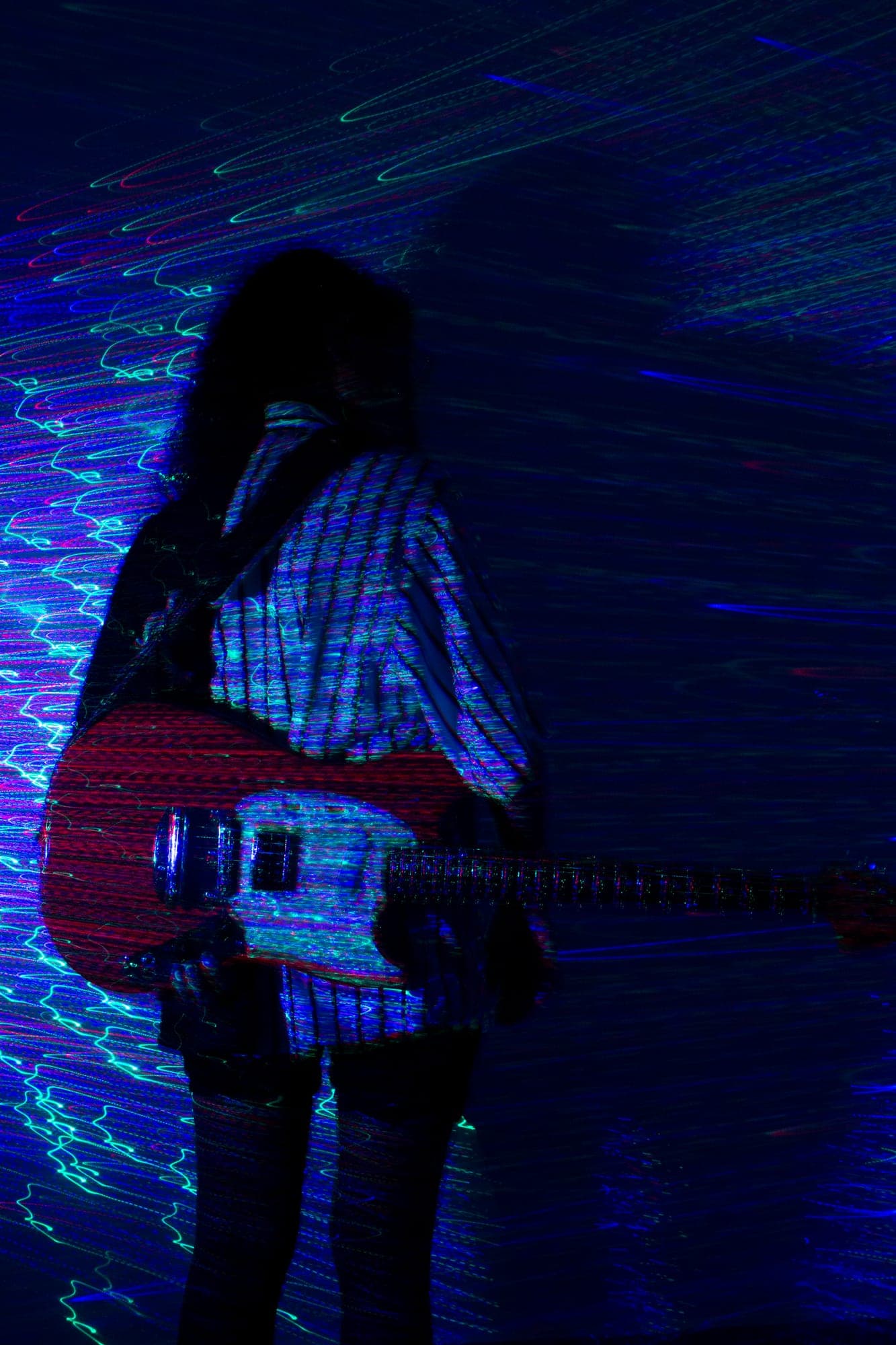 Exposición larga: silueta con una guitarra eléctrica mientras las estelas de luz azul y roja recorren el cuerpo.