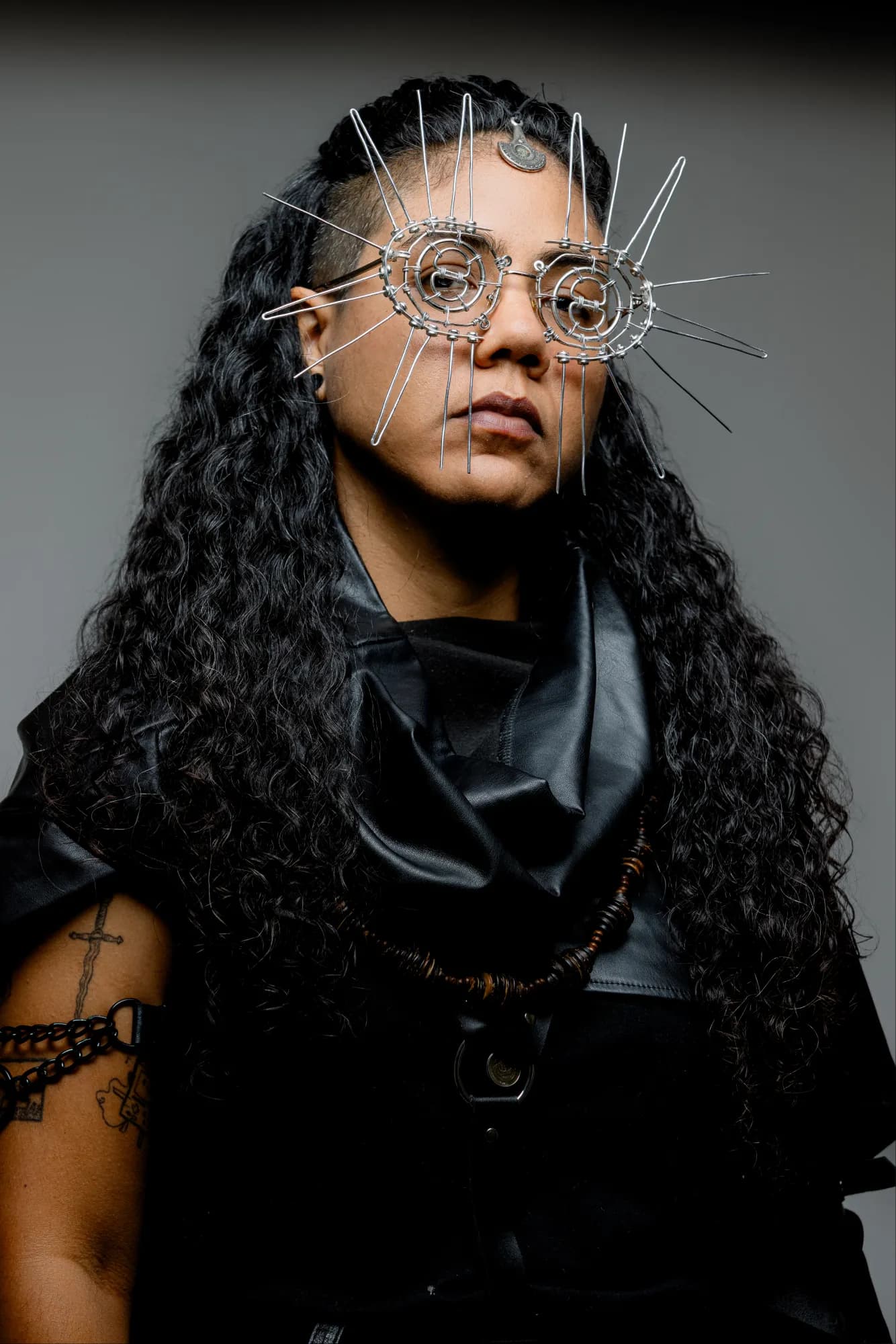 Maria Lunares con unas gafas de alambre rematadas en púas que salen como rayos de sol, melena rizada suelta y cuero negro.